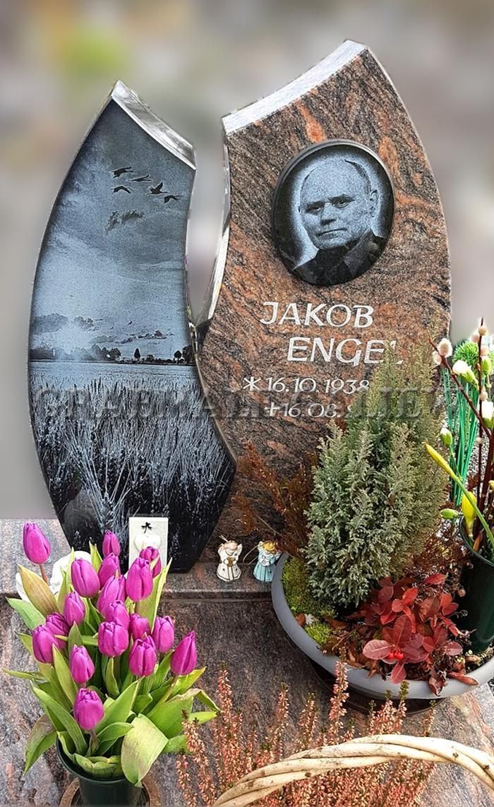 Ein Grabstein mit dem Bild eines Mannes ist von Blumen umgeben.