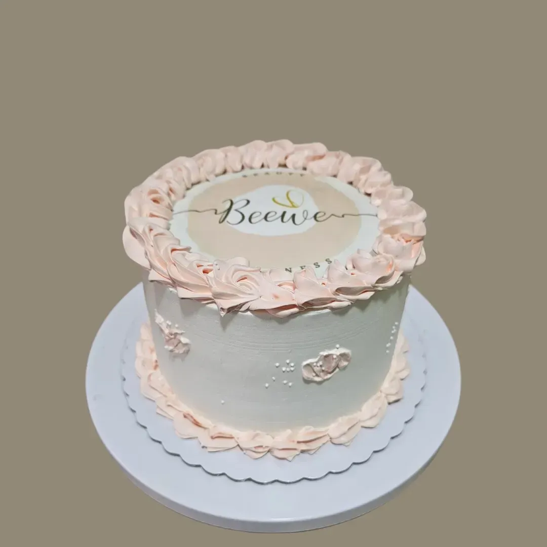 Pastel blanco con glaseado rosa, logotipo de Beewe en la parte superior y flores decorativas.