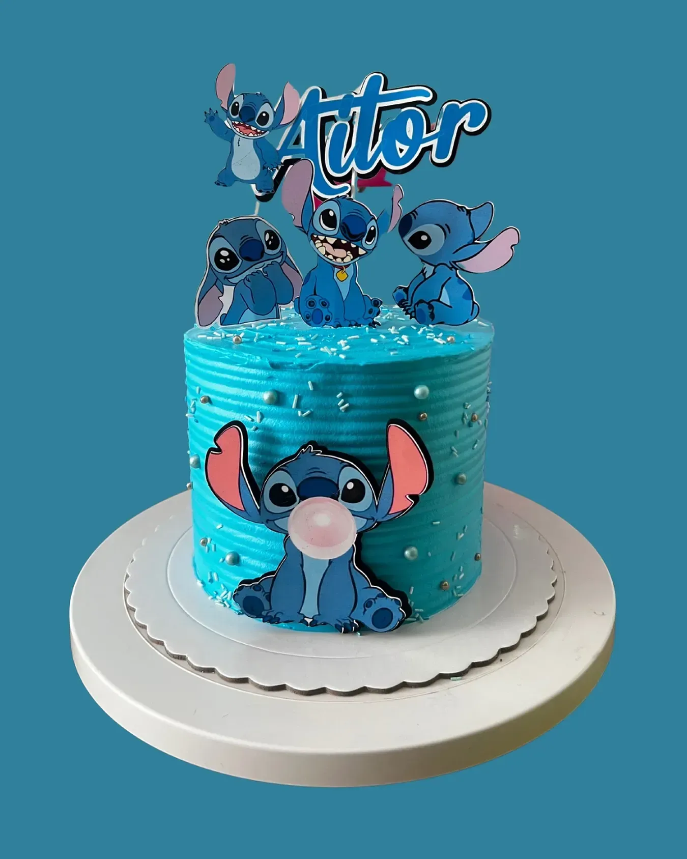 Pastel decorado con personajes de Stitch, glaseado azul y adorno con la palabra