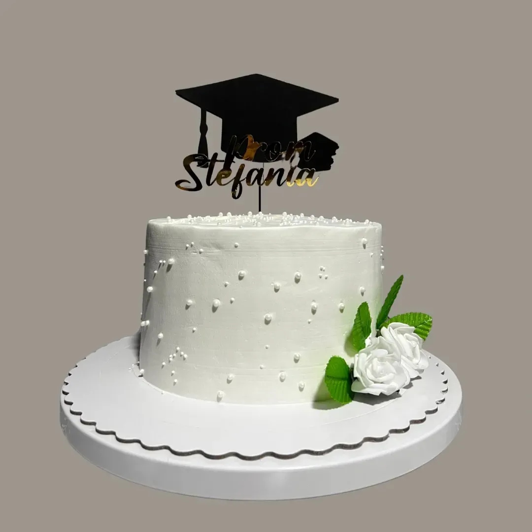 Tarta de graduación blanca con birrete y flores; lleva el nombre de Stefanía.