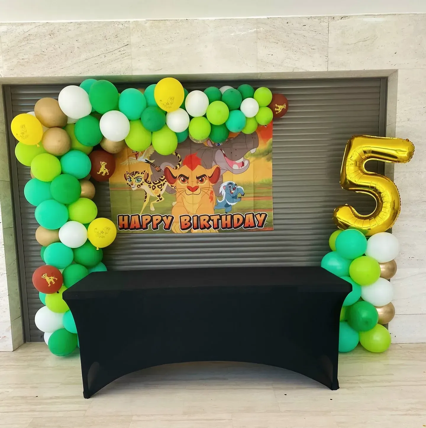 Montaje de fiesta de cumpleaños con temática de la Guardia del León: arco de globos, mesa, telón de fondo y globo con el número