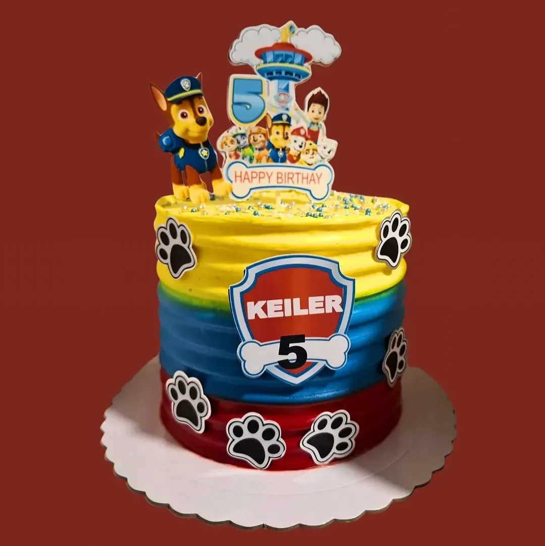 Tarta de cumpleaños temática de Paw Patrol con figura de Chase, huellas de patas y texto personalizado.