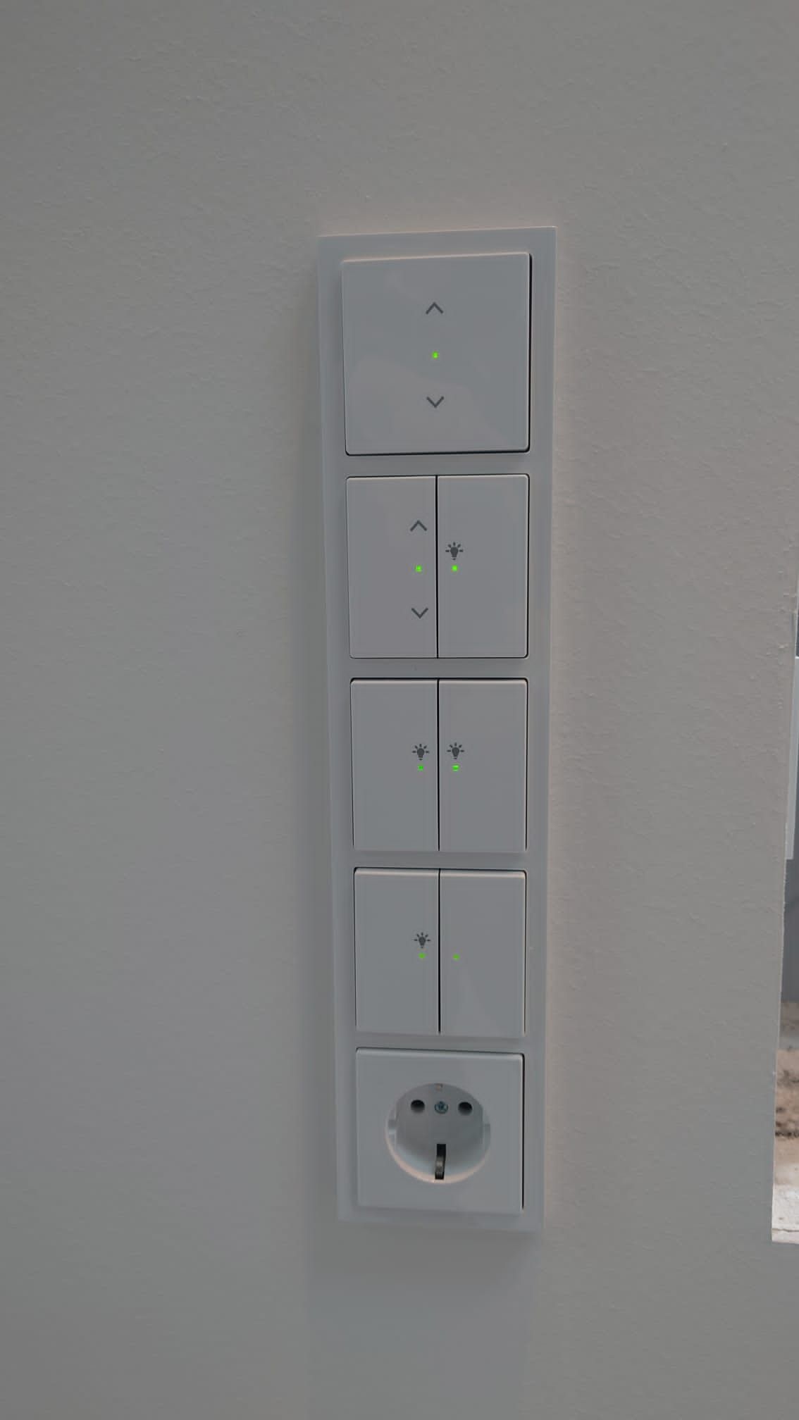 Eine weiße Wand mit einer vertikalen Reihe von Lichtschaltern und einer Steckdose.