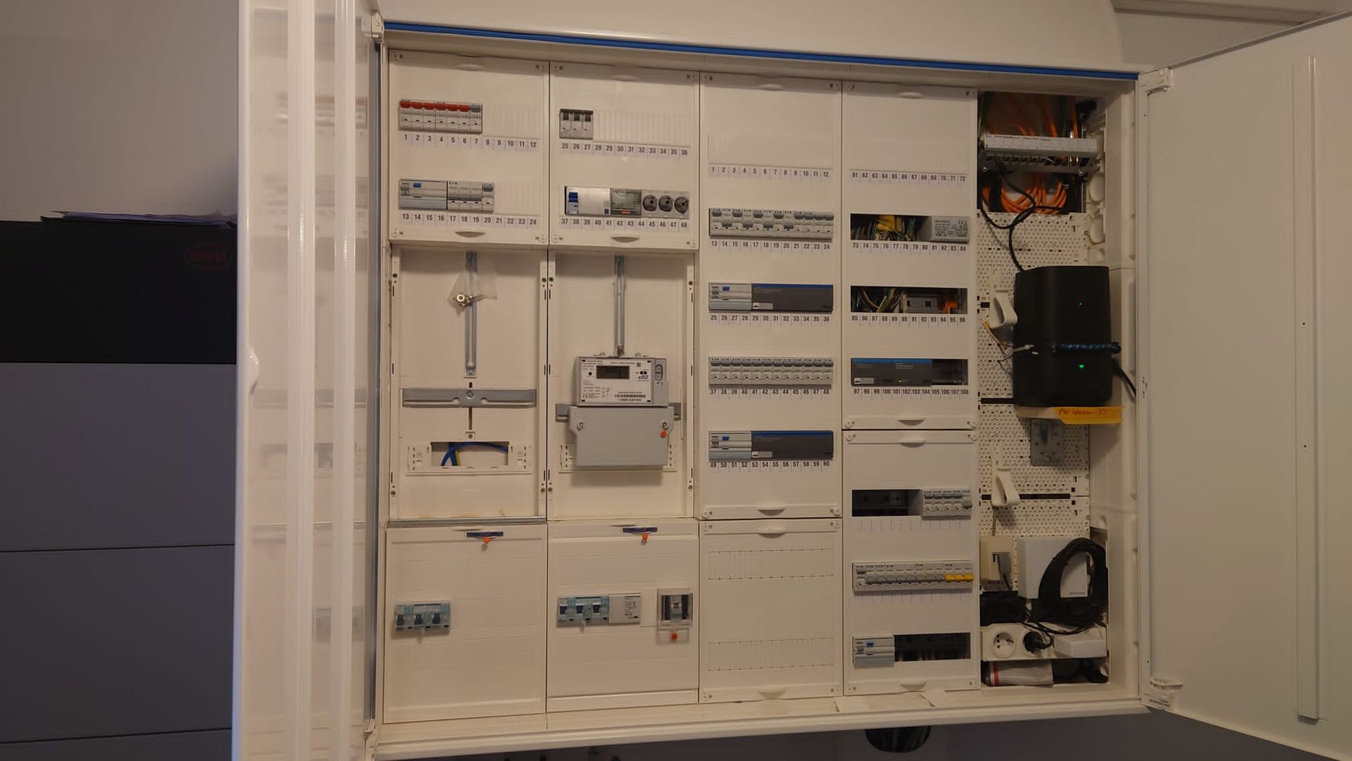 Weiße Schalttafel mit verschiedenen Leistungsschaltern, Messgeräten und Verkabelung in einem Schrank.