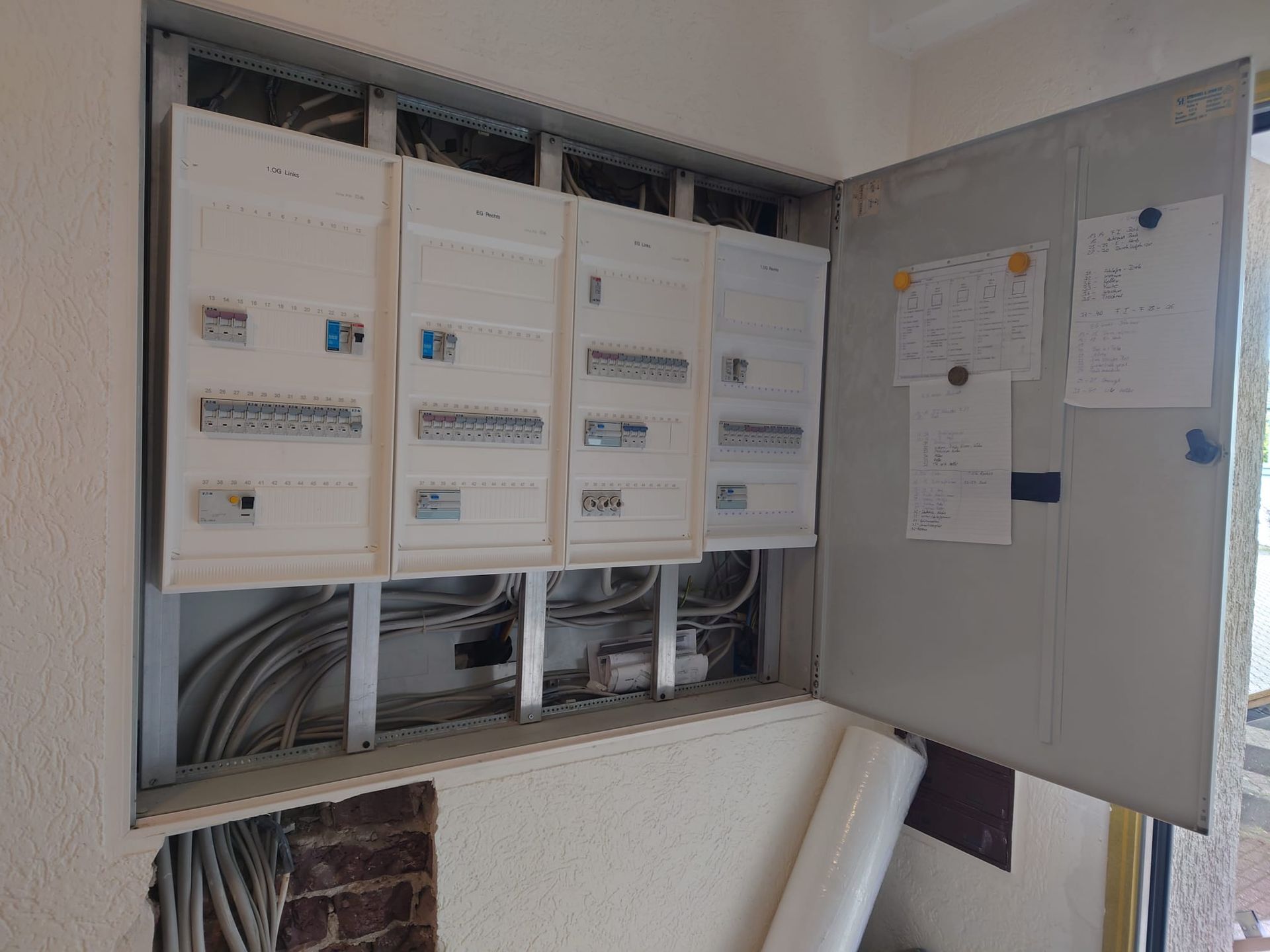 In einer Wand sind Schalttafeln installiert, eine Tür ist offen und mit Papieren bestückt.