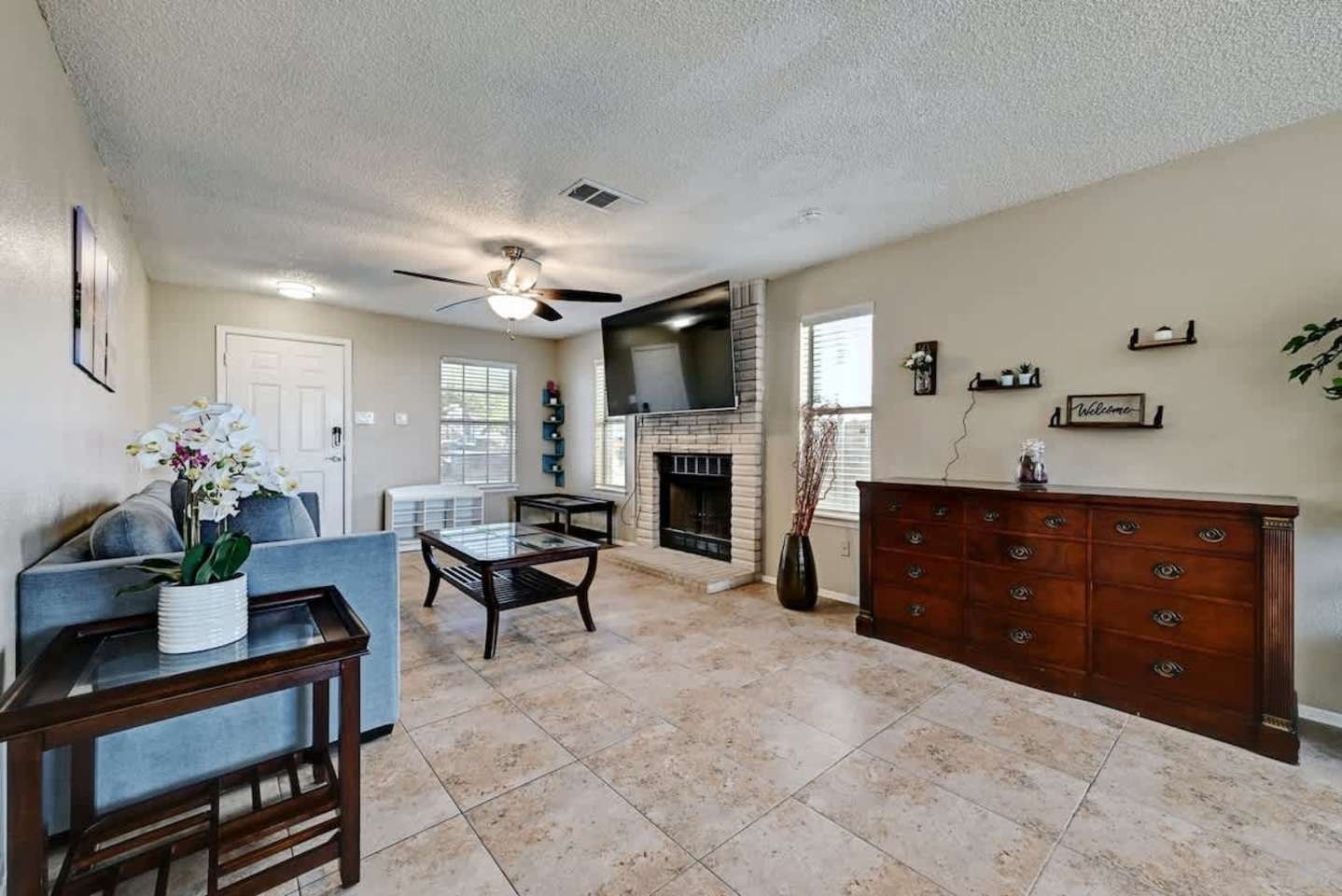 Bright living room with tile floor, fireplace, TV, sofa, and wooden sideboard under a ceiling fan