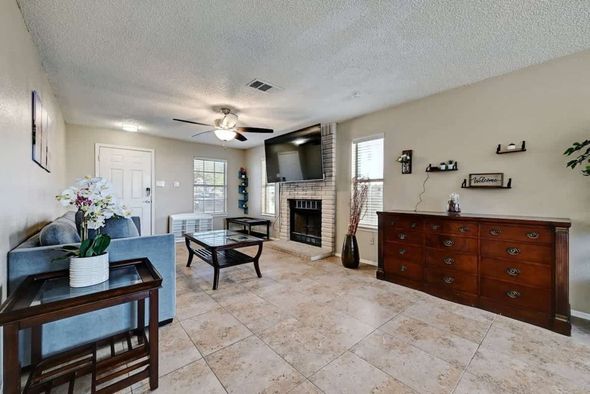 Bright living room with tile floor, fireplace, TV, sofa, and wooden sideboard under a ceiling fan
