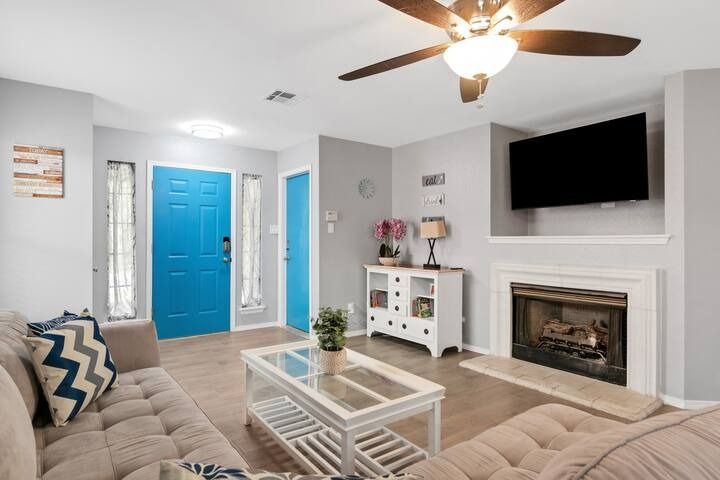 Bright living room with teal front door, mounted TV, fireplace, and beige sofa.