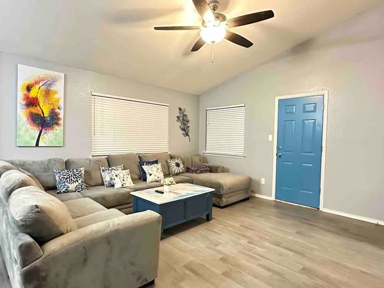 Cozy living room with gray sectional sofa, blue door, ceiling fan, and light wood flooring