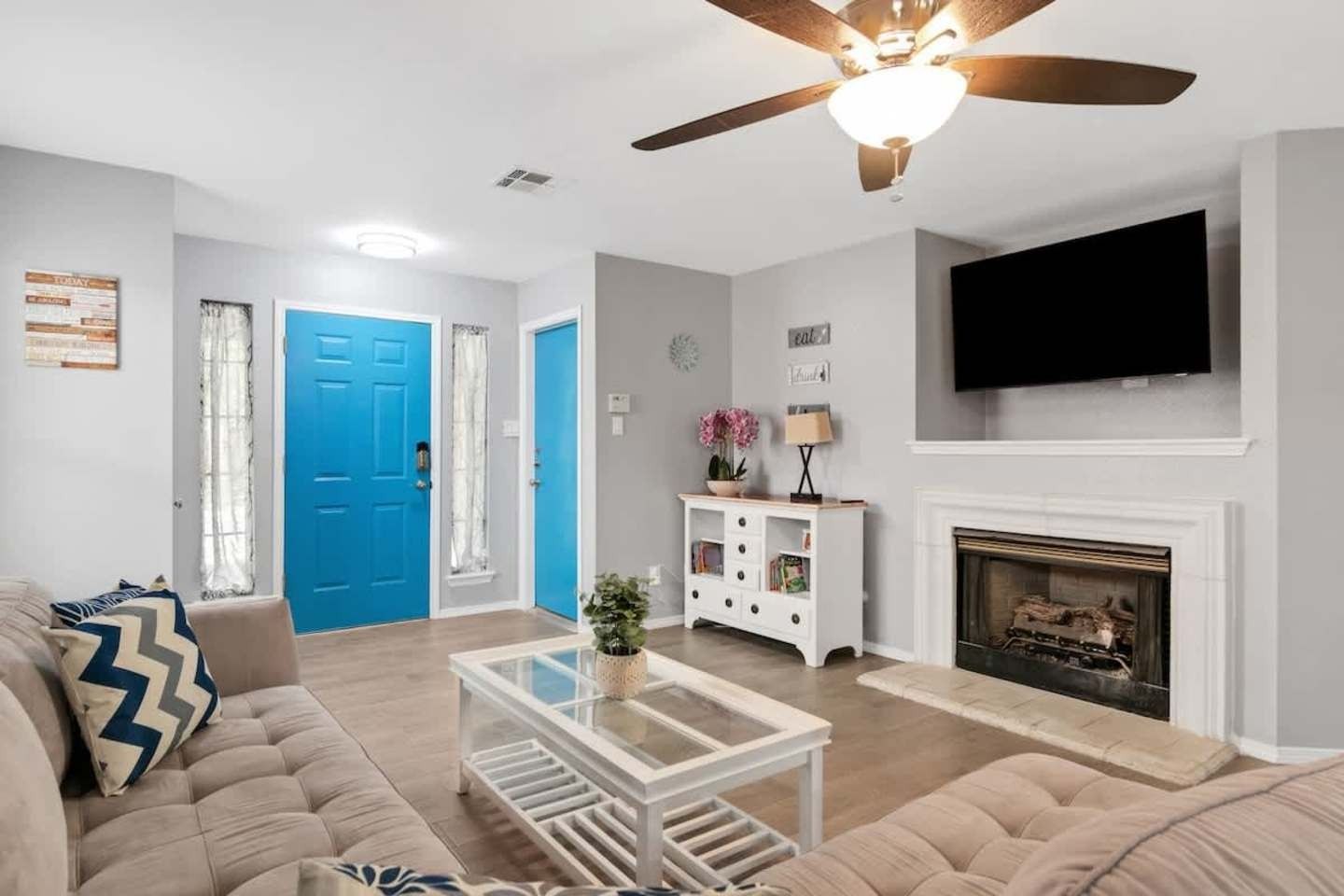 Bright living room with blue front door, white fireplace, wall-mounted TV, and beige sectional sofa