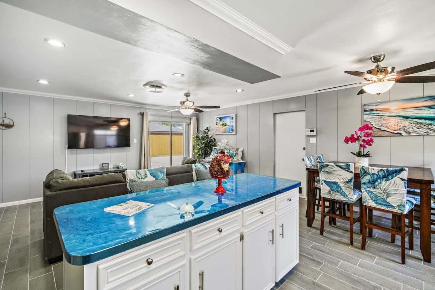 Bright modern kitchen and living area with blue island countertop, gray cabinets, and dining table