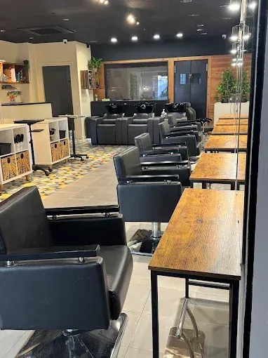 Interior de peluquería con estaciones de peinado, sillas negras y lavabos al fondo.