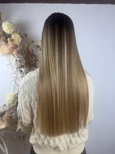 Mujer con cabello largo y liso, con degradado de castaño oscuro a rubio, vistiendo un suéter de punto cable de color crema.