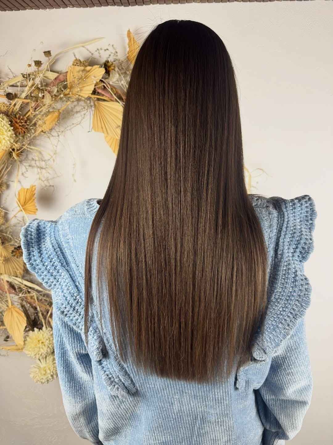 Mujer con cabello castaño largo y liso, vistiendo un suéter azul claro con hombros fruncidos, frente a un fondo neutro.