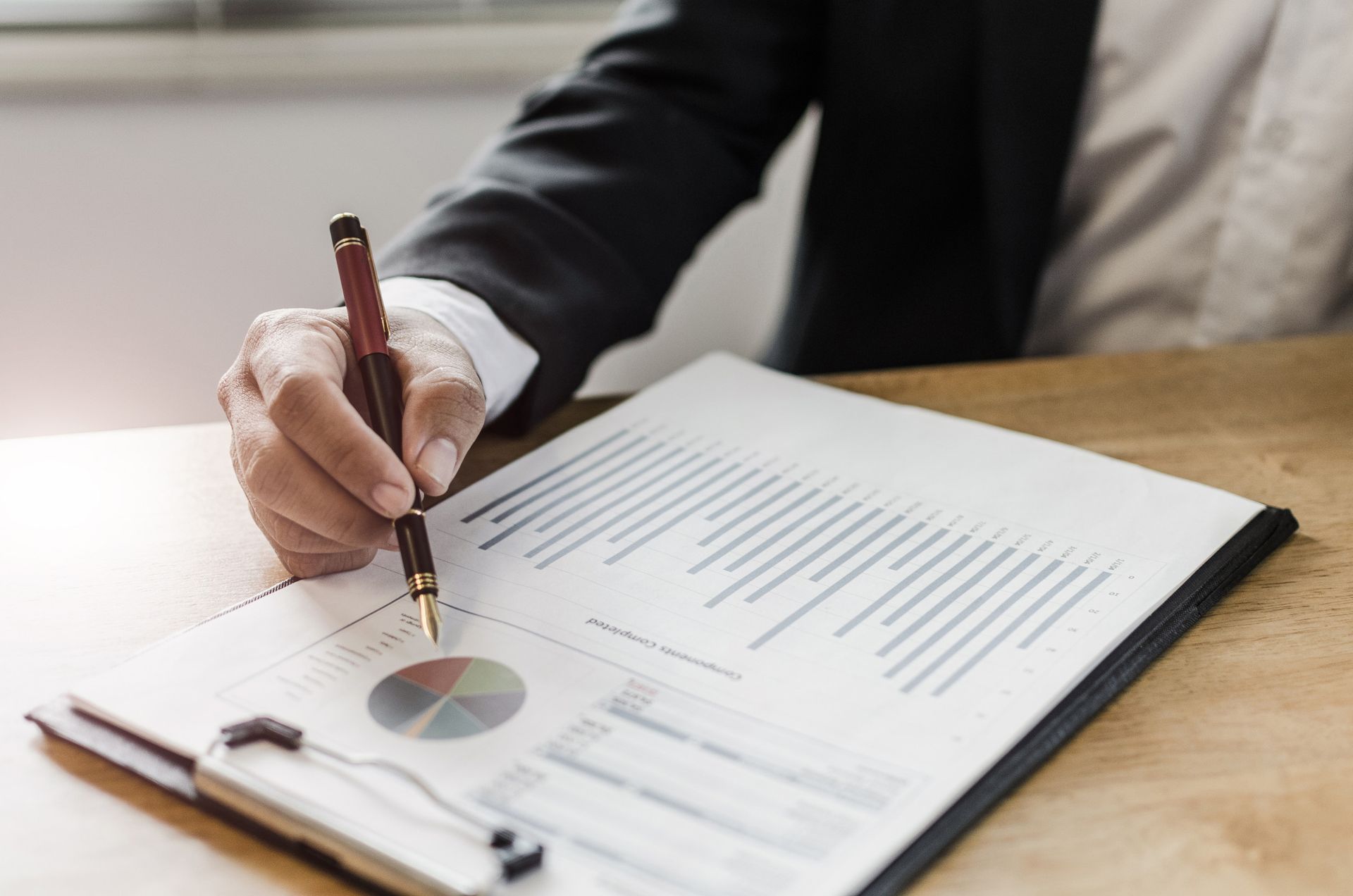 Una persona vestida de traje revisa un informe financiero con un bolígrafo, señalando un gráfico en un portapapeles.