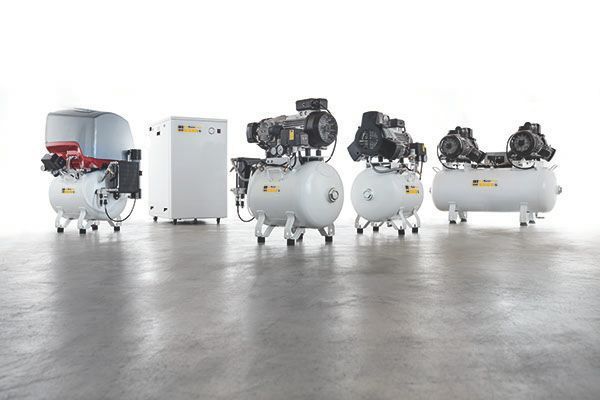 Fünf weiße Dentalkompressoren in verschiedenen Größen, auf einem hellgrauen Boden.