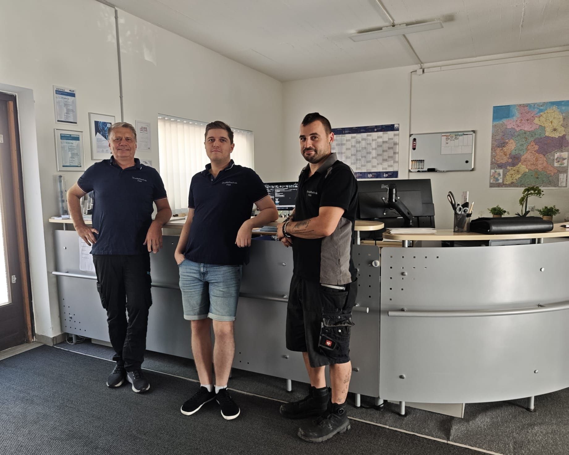 Das Team von Drucklufttechnik Frick steht vor dem Empfangstresen in ihrem Büro in Olching. 