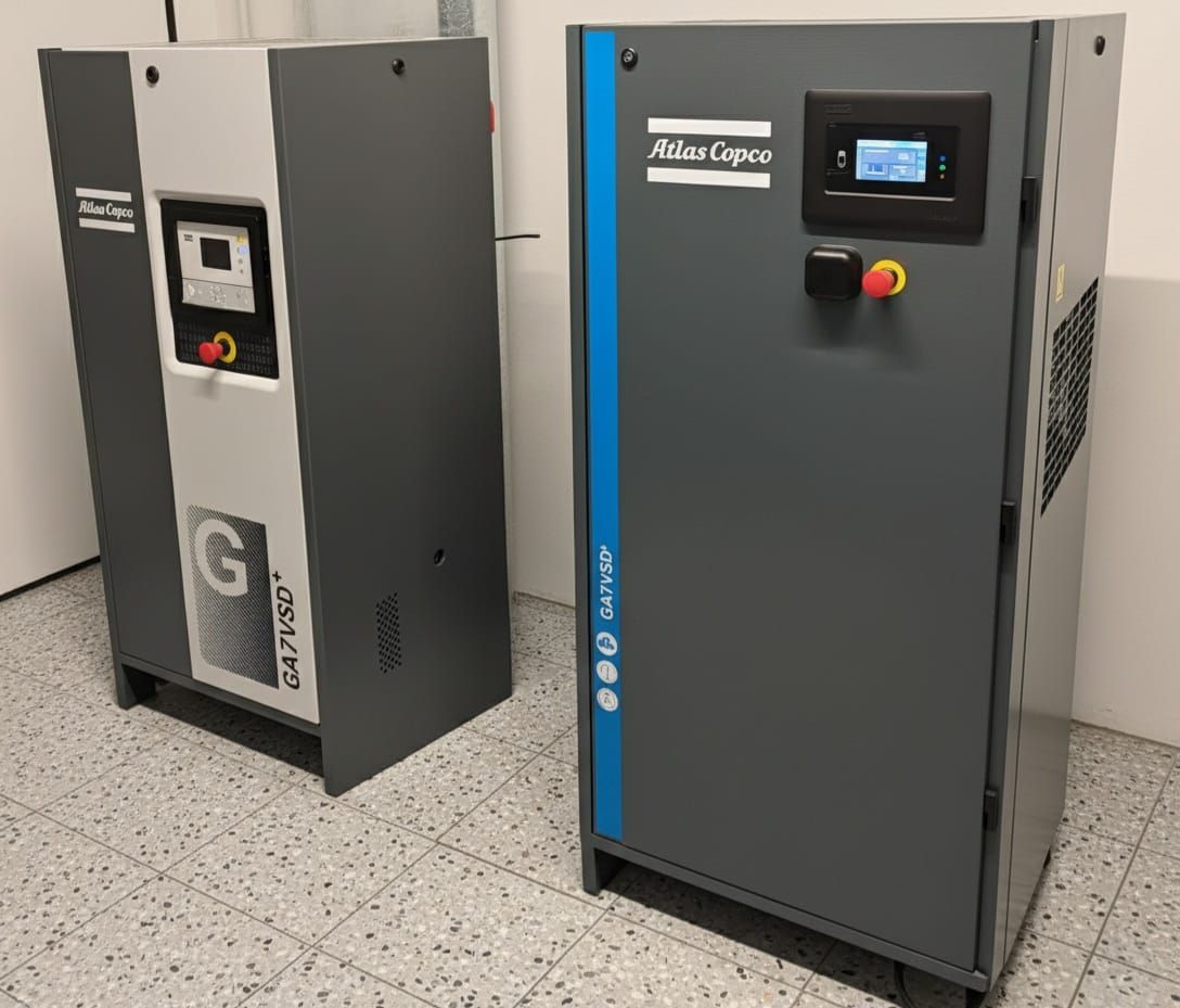 Zwei graue Atlas Copco Luftkompressoren in einem weißen Raum, einer davon mit blauen Akzenten.