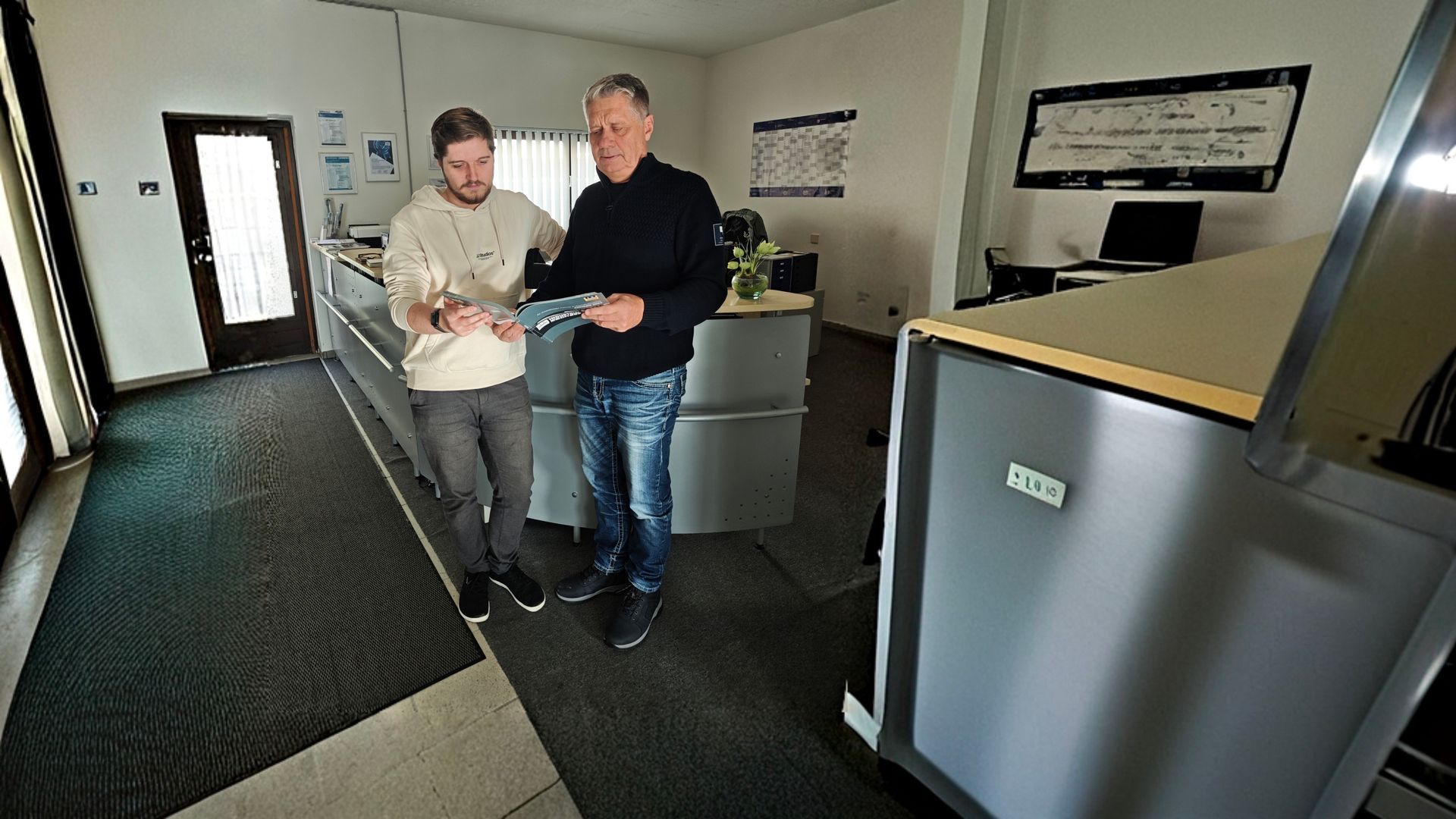 Herr Frick und ein Kollege blättern in einem Katalog - Vertrieb von Kompressoren und mehr.