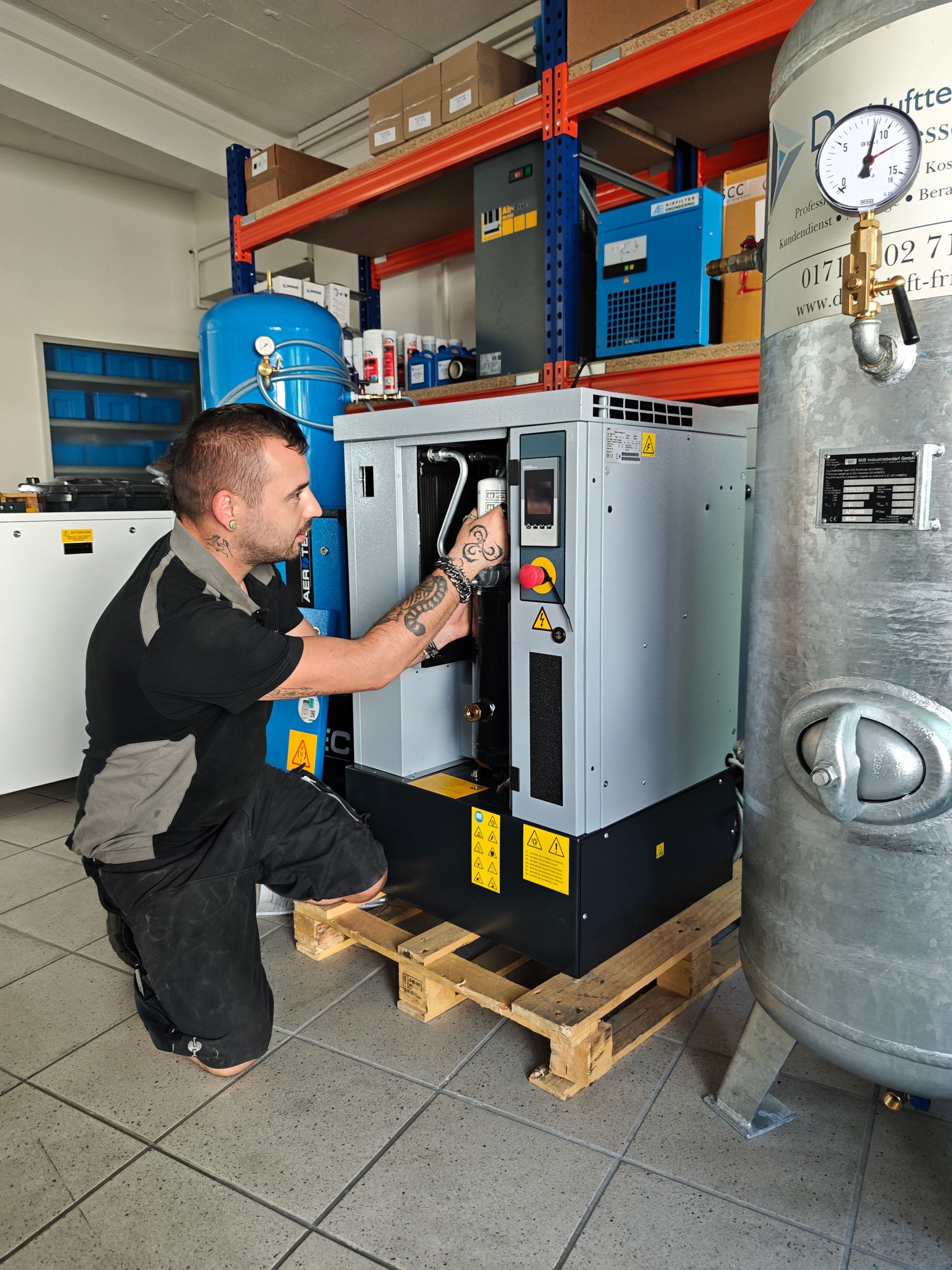 Ein Mechaniker arbeitet an einem industriellen Luftkompressor. Er kniet in einer Werkstatt neben der Maschine.