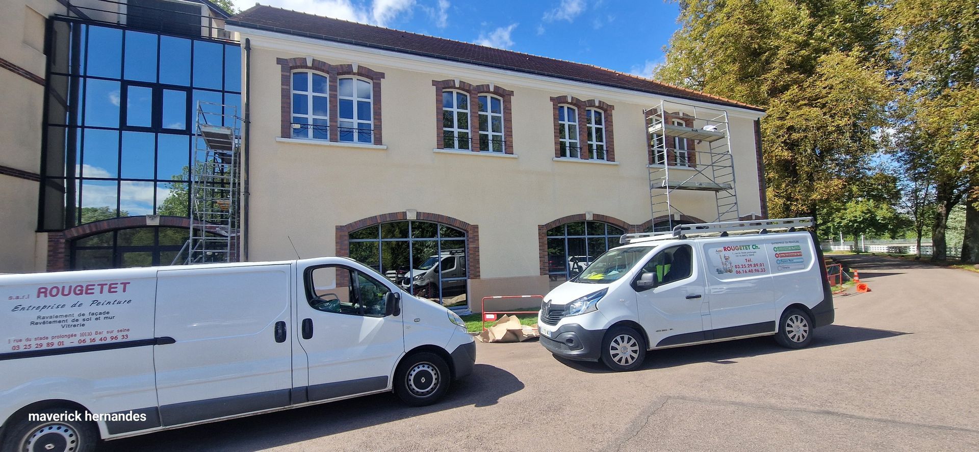 Des fourgonnettes de service blanches garées devant un bâtiment beige aux grandes fenêtres par une journée ensoleillée.