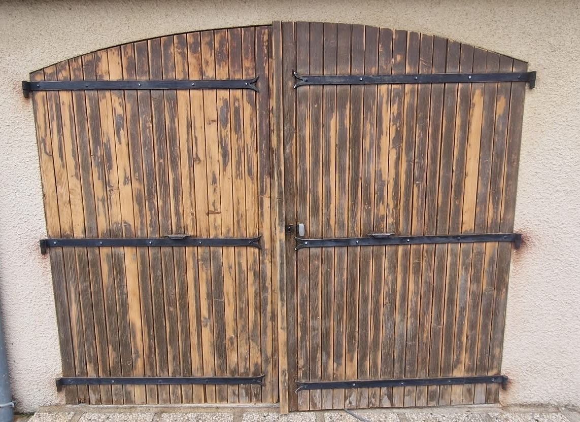 Portail double en bois patiné, à charnières noires, adossé à un mur en stuc.