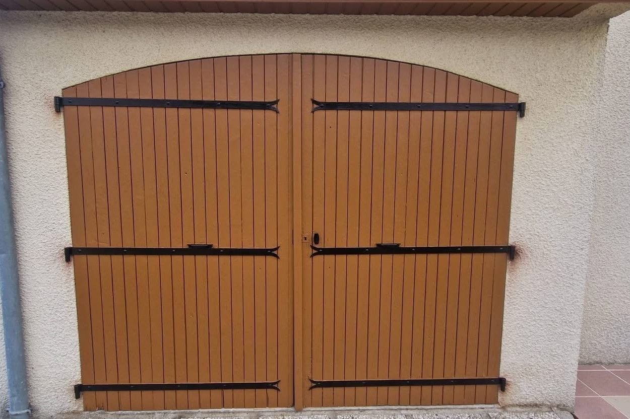 Portail double fermé en bois brun orangé avec charnières en métal noir sur un mur en stuc.