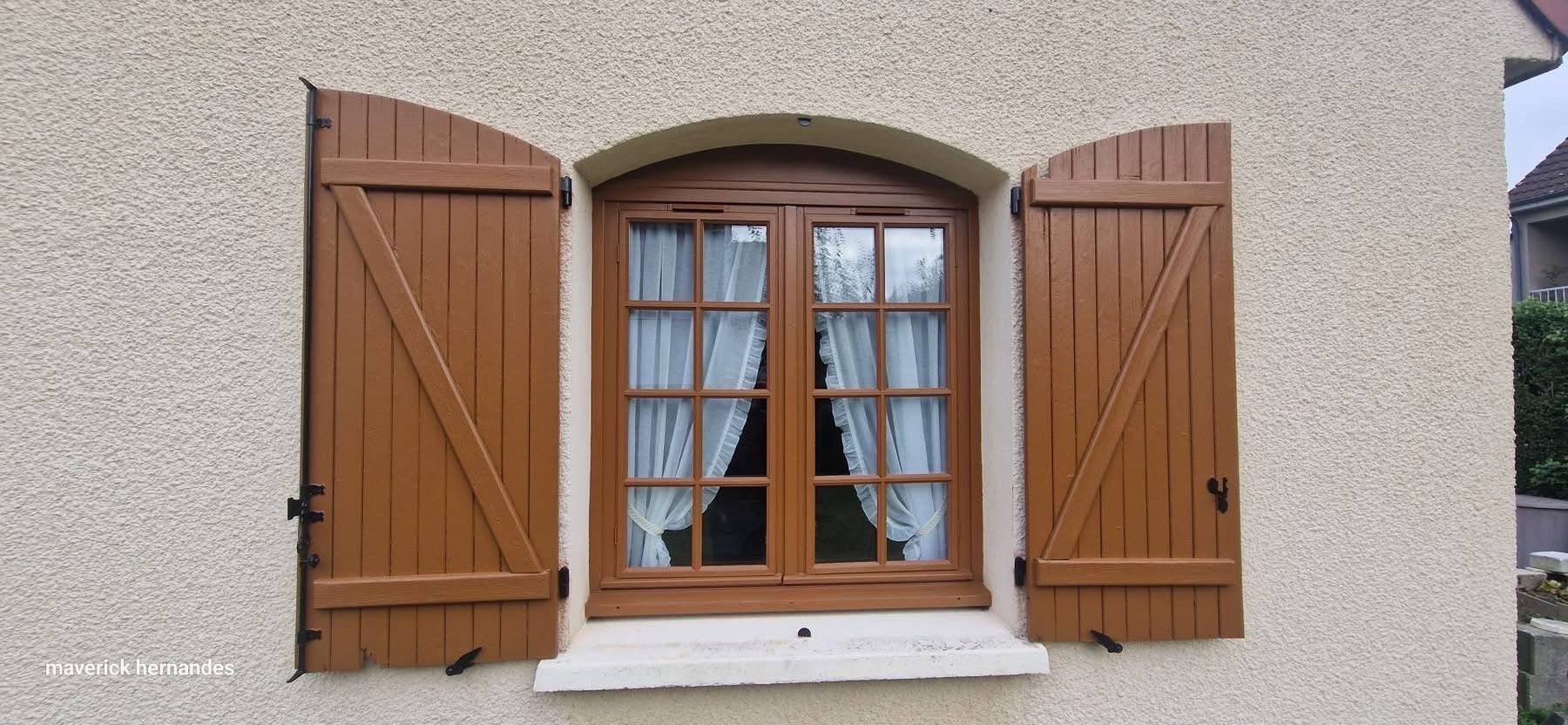 Fenêtre en bois avec volets bruns sur un mur en stuc beige.