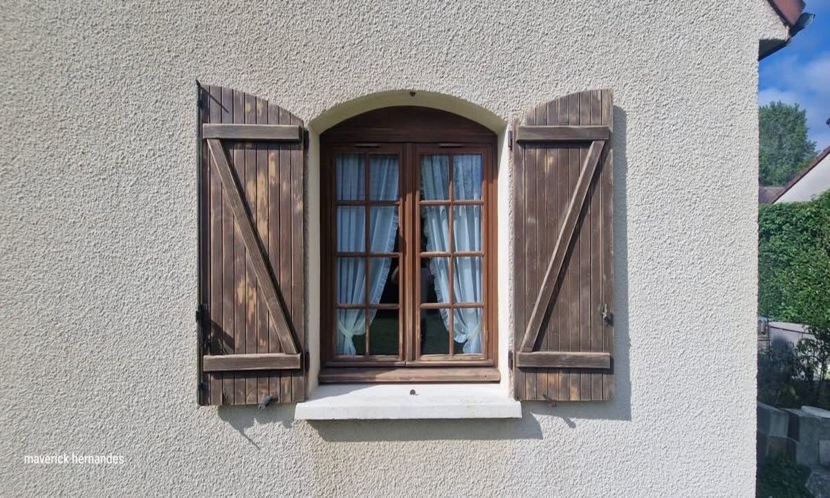 Fenêtre à volets en bois avec rideaux bleus sur l'extérieur d'une maison en stuc.