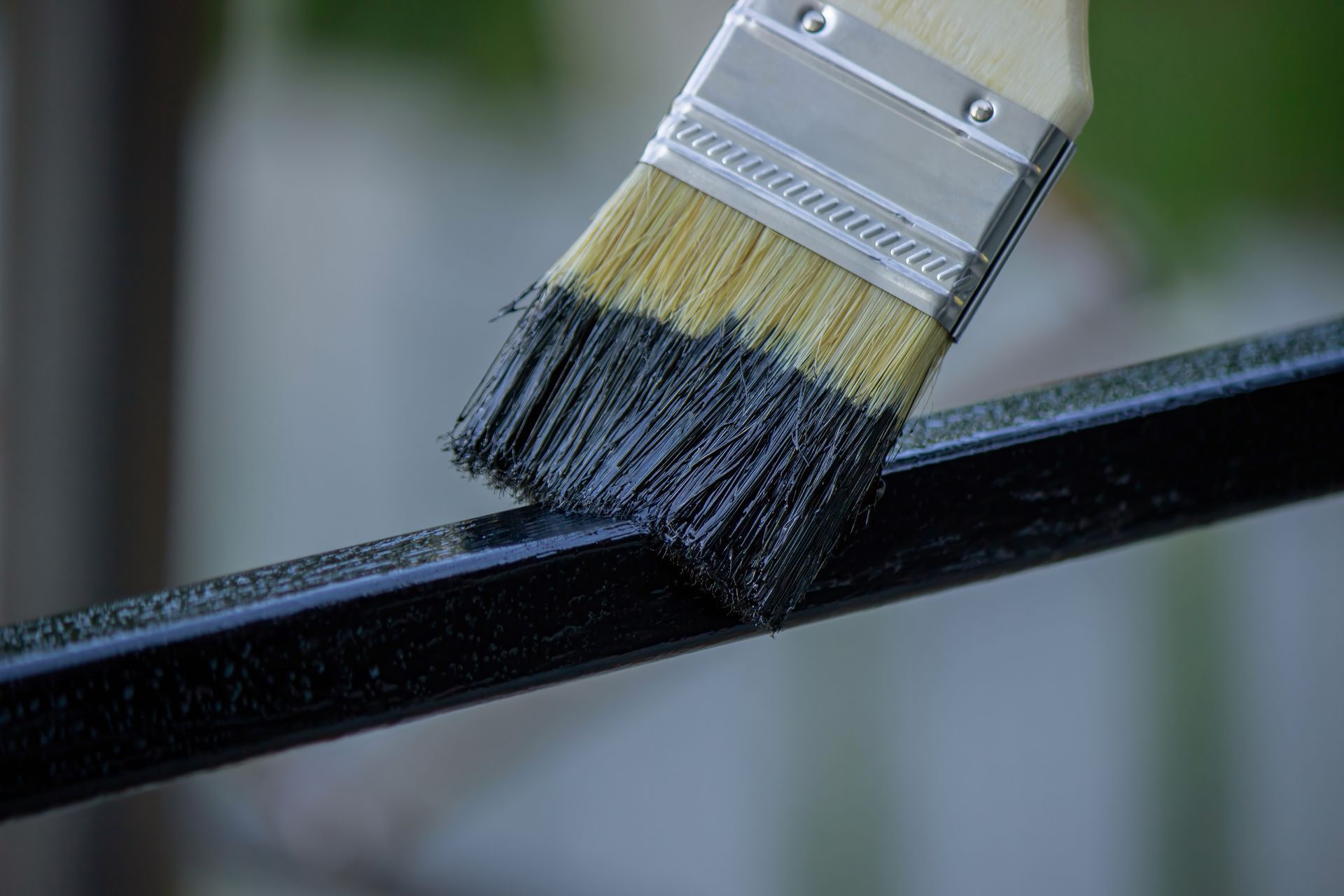 Un pinceau applique de la peinture noire sur un rail métallique.