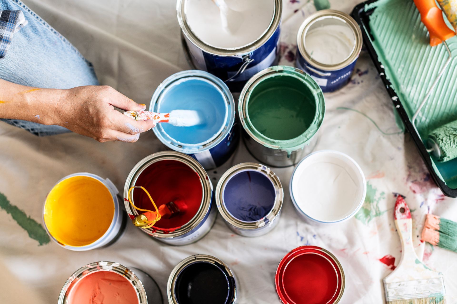 Vue de dessus de pots de peinture ouverts contenant des peintures colorées et d'une main remuant de la peinture bleue avec un pinceau.