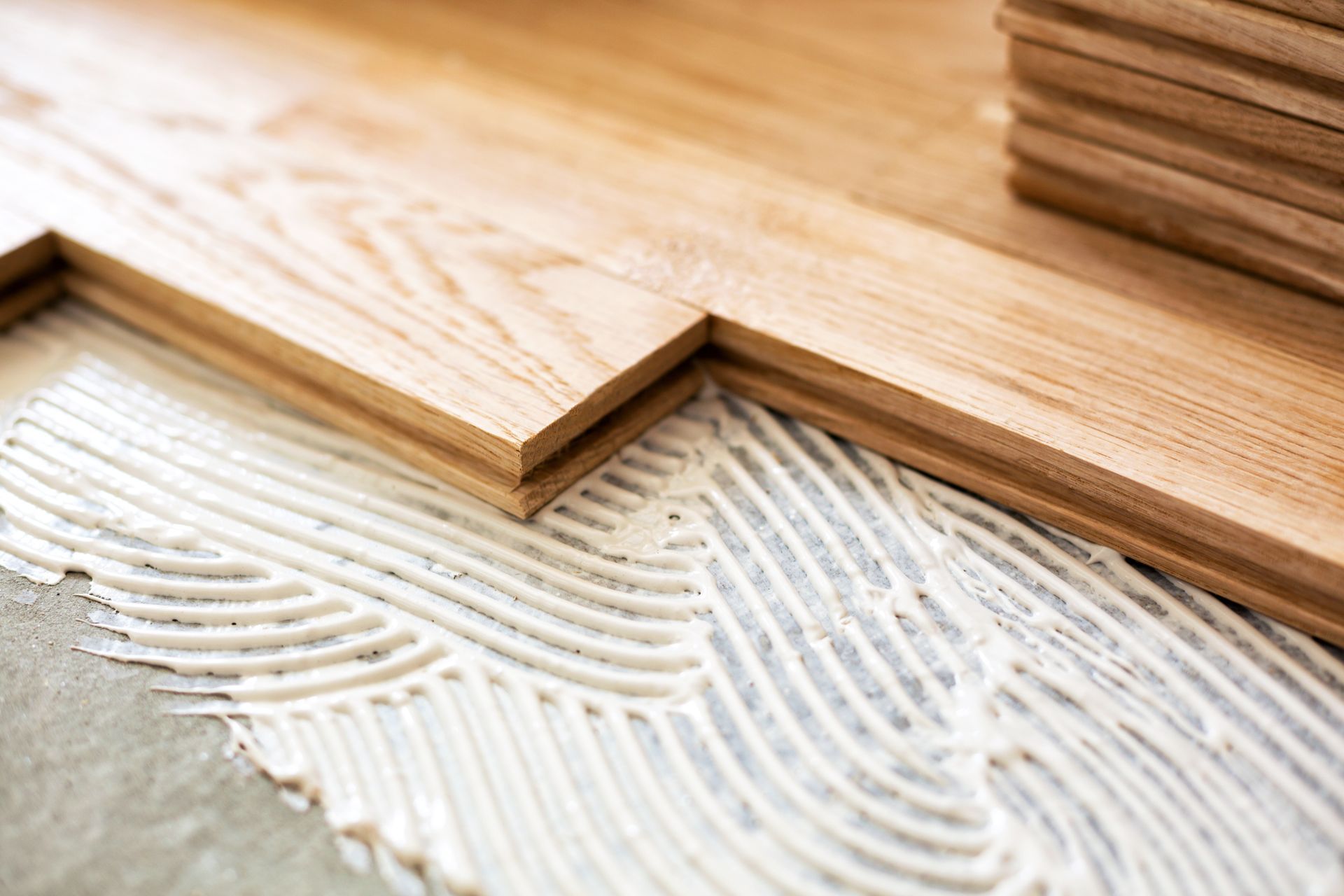 Pose de lames de parquet sur de la colle blanche avec des stries de truelle.
