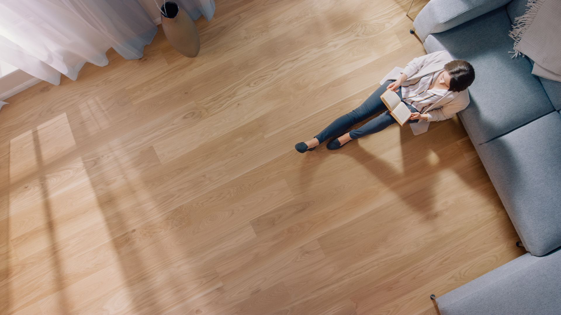 Une personne allongée sur un canapé gris dans une pièce lumineuse avec un parquet clair.