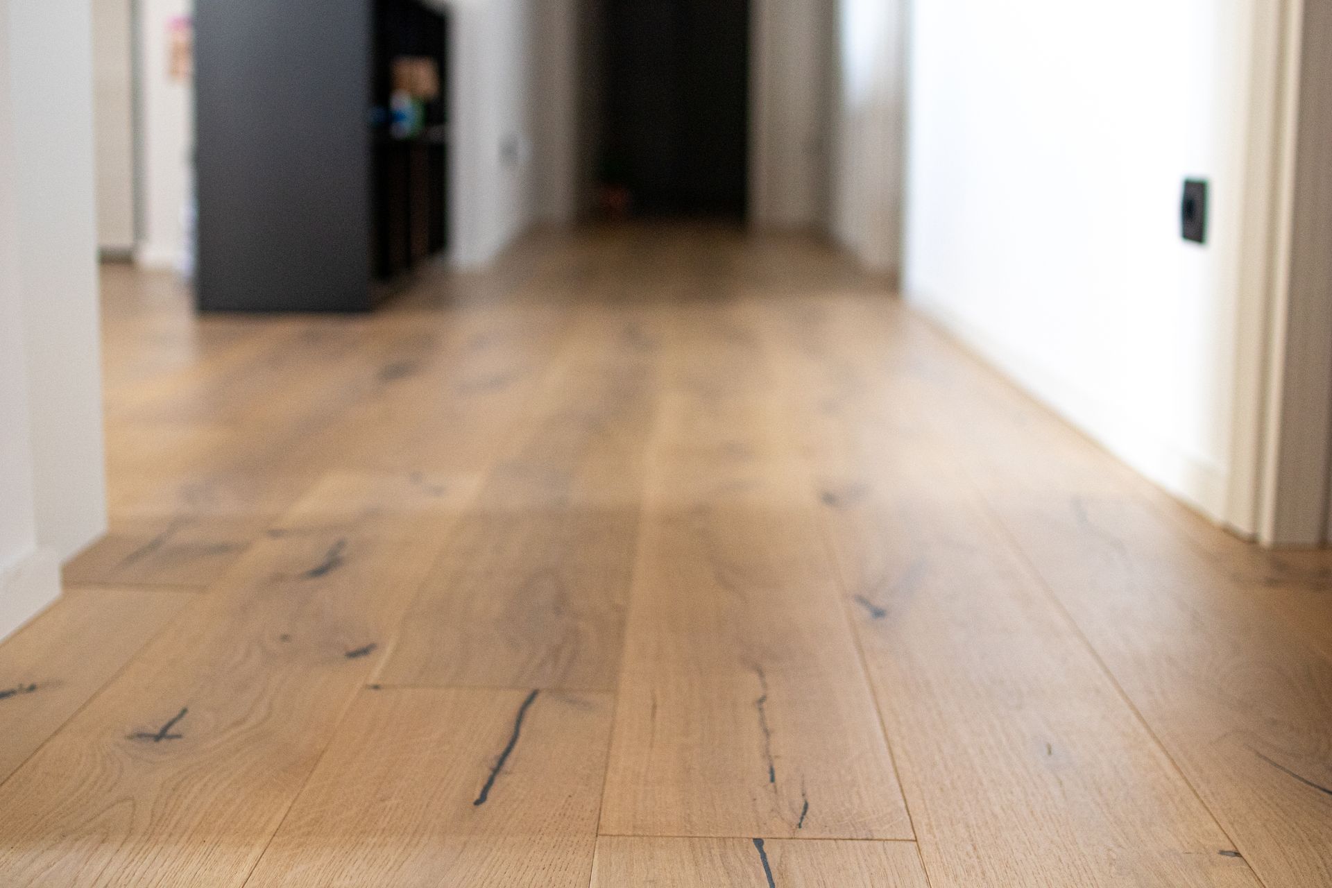 Couloir vide avec parquet clair et murs blancs.
