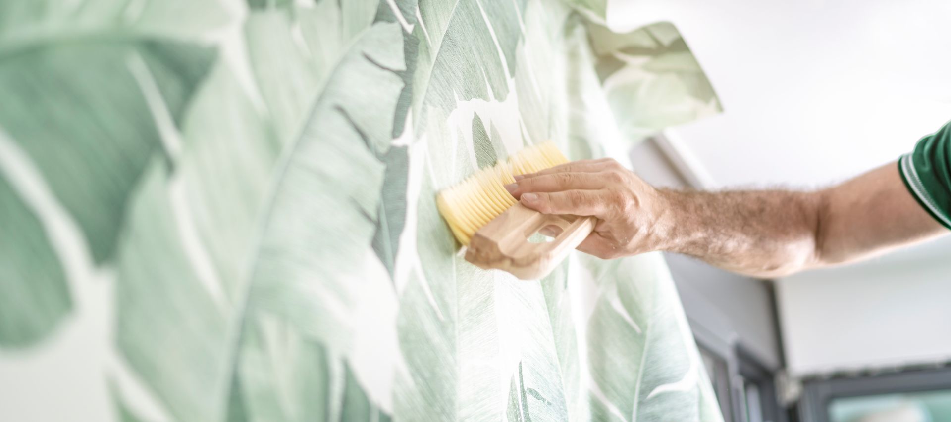 Peinture à la main d'un mur blanc avec un rouleau de peinture jaune sur un motif de feuilles vert menthe.