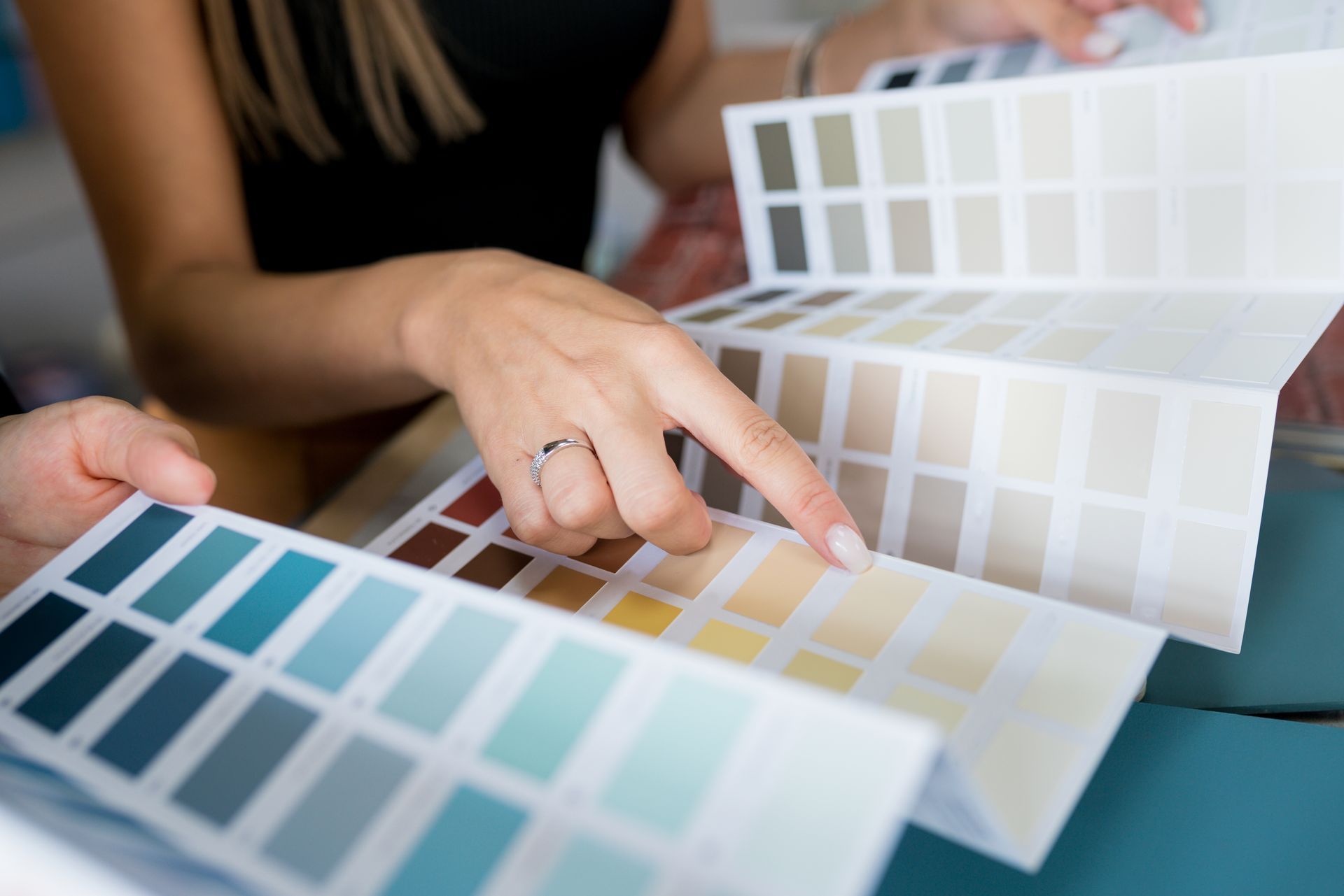Des mains pointent du doigt des échantillons de peinture et des nuanciers sur une table.