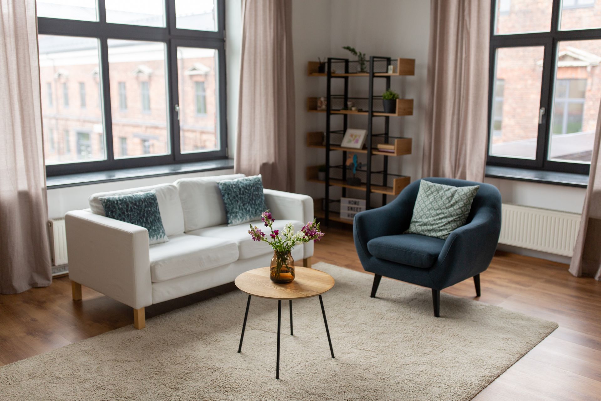 Salon lumineux avec canapé blanc, fauteuil bleu, table basse ronde et grandes fenêtres.