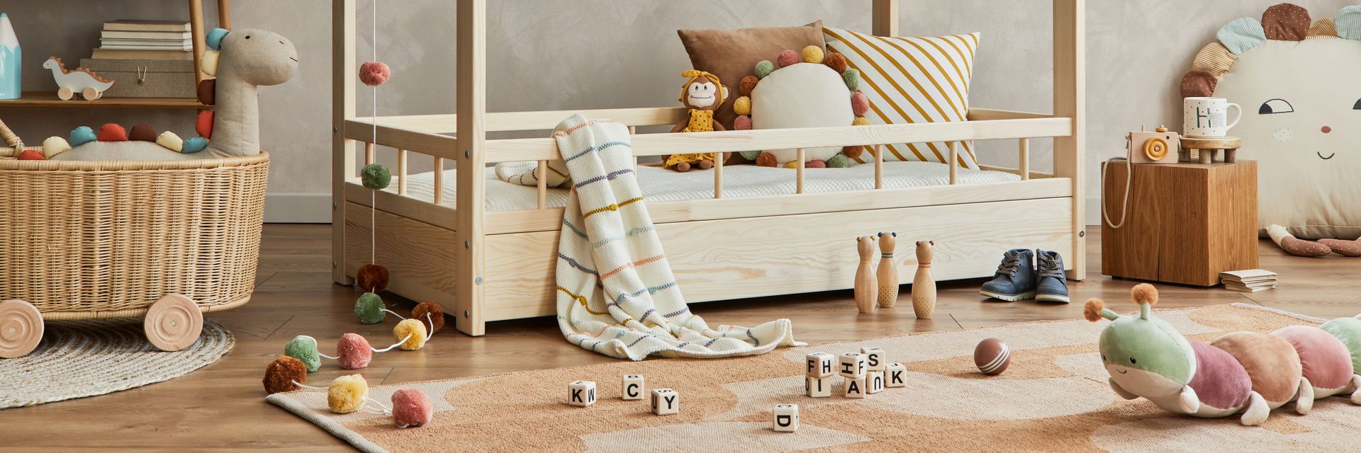 Chambre d'enfant confortable avec un berceau, un canapé beige, un panier en osier et des jouets éparpillés sur un sol en bois.