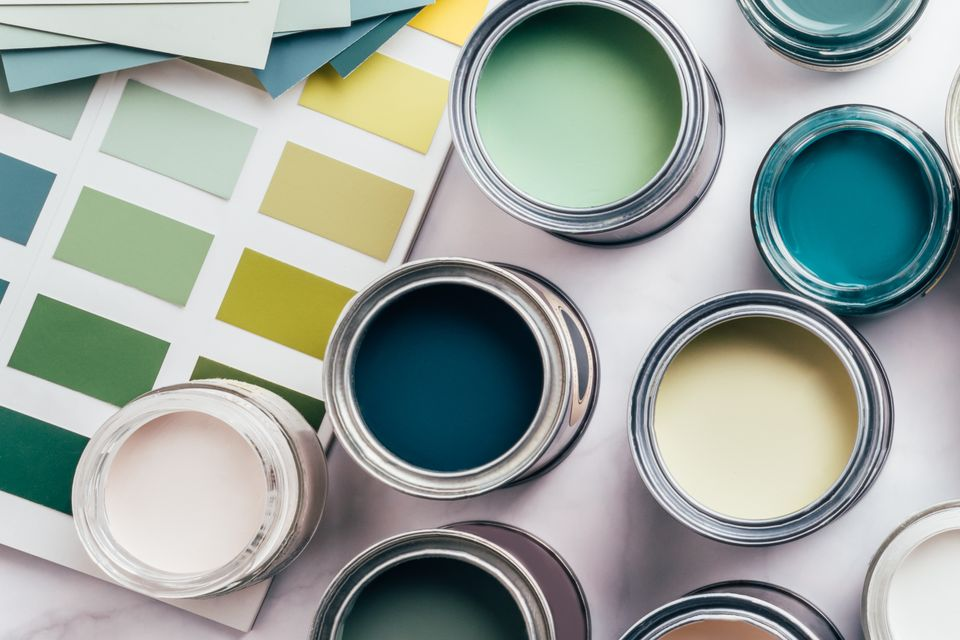 Des pots de peinture ouverts de couleur turquoise, verte et crème sont placés à côté d'échantillons de couleurs sur une surface blanche.