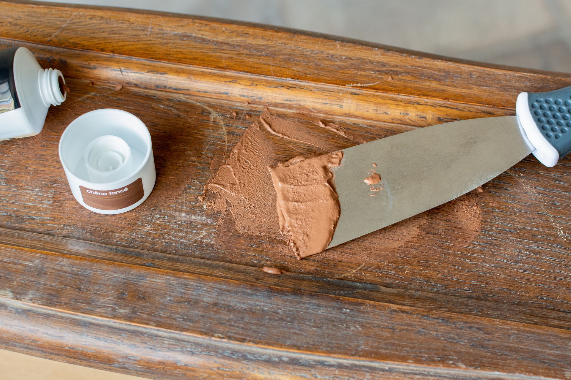 Tube de pâte brune et spatule métallique sur un plateau en bois avec deux couvercles ouverts.