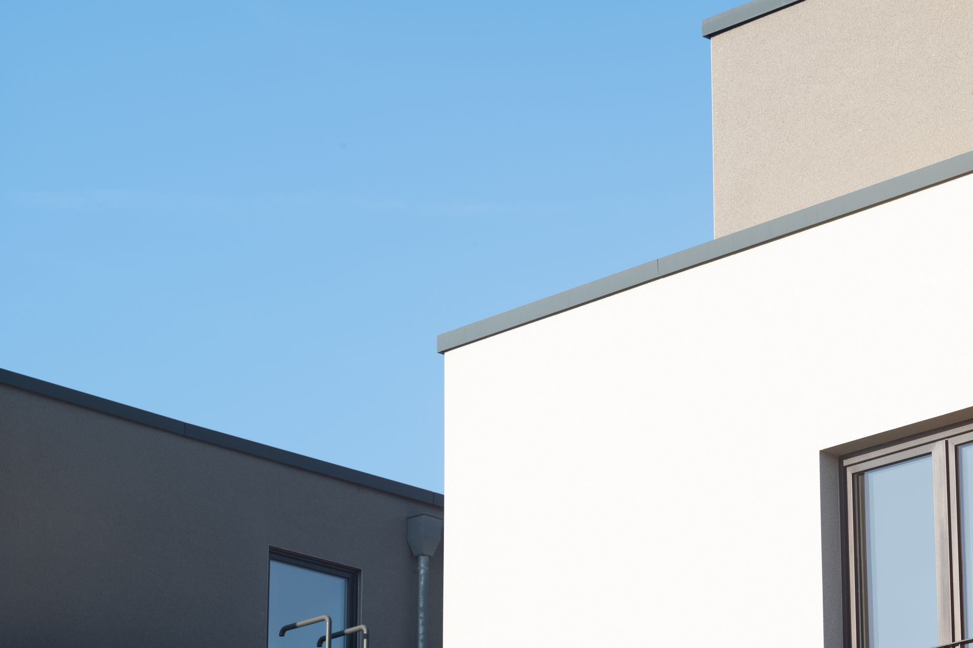 Façades d'immeubles modernes aux murs blancs et gris sous un ciel d'un bleu limpide.
