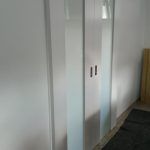 ein Flur mit einer Glasschiebetür zwischen zwei weißen Wänden. Schreinerei Molitor