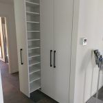 ein weißer Schrank mit Regalen und Türen in einem Flur.