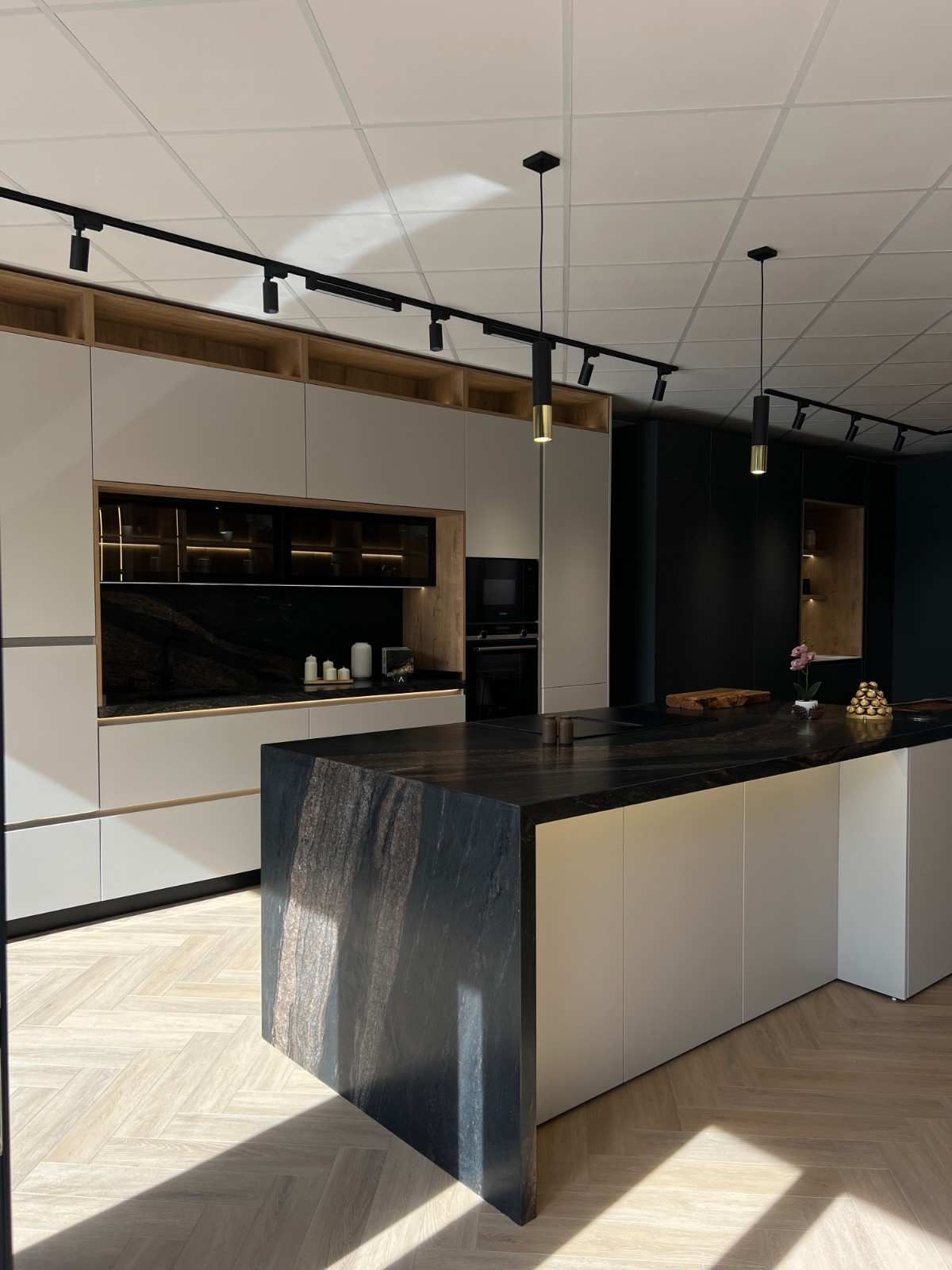 Cocina moderna con isla negra, armarios blancos y techos altos con iluminación de riel.