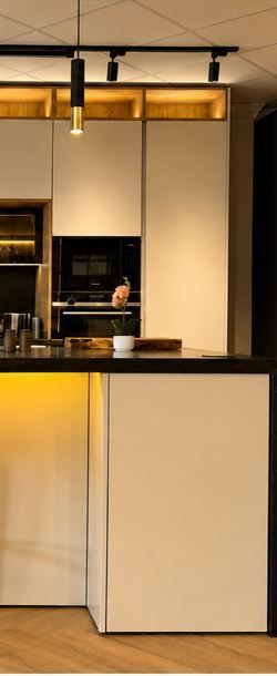 Interior de cocina moderno con gabinetes color crema, iluminación cálida y lámparas colgantes negras sobre la encimera.