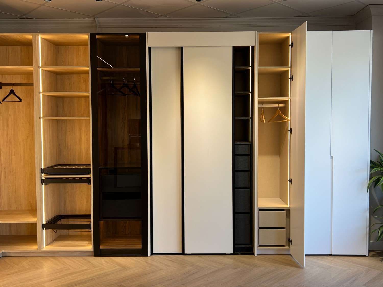 Armario abierto de madera con estantes, barras para colgar ropa, cajones y puertas correderas con espejo en un dormitorio.