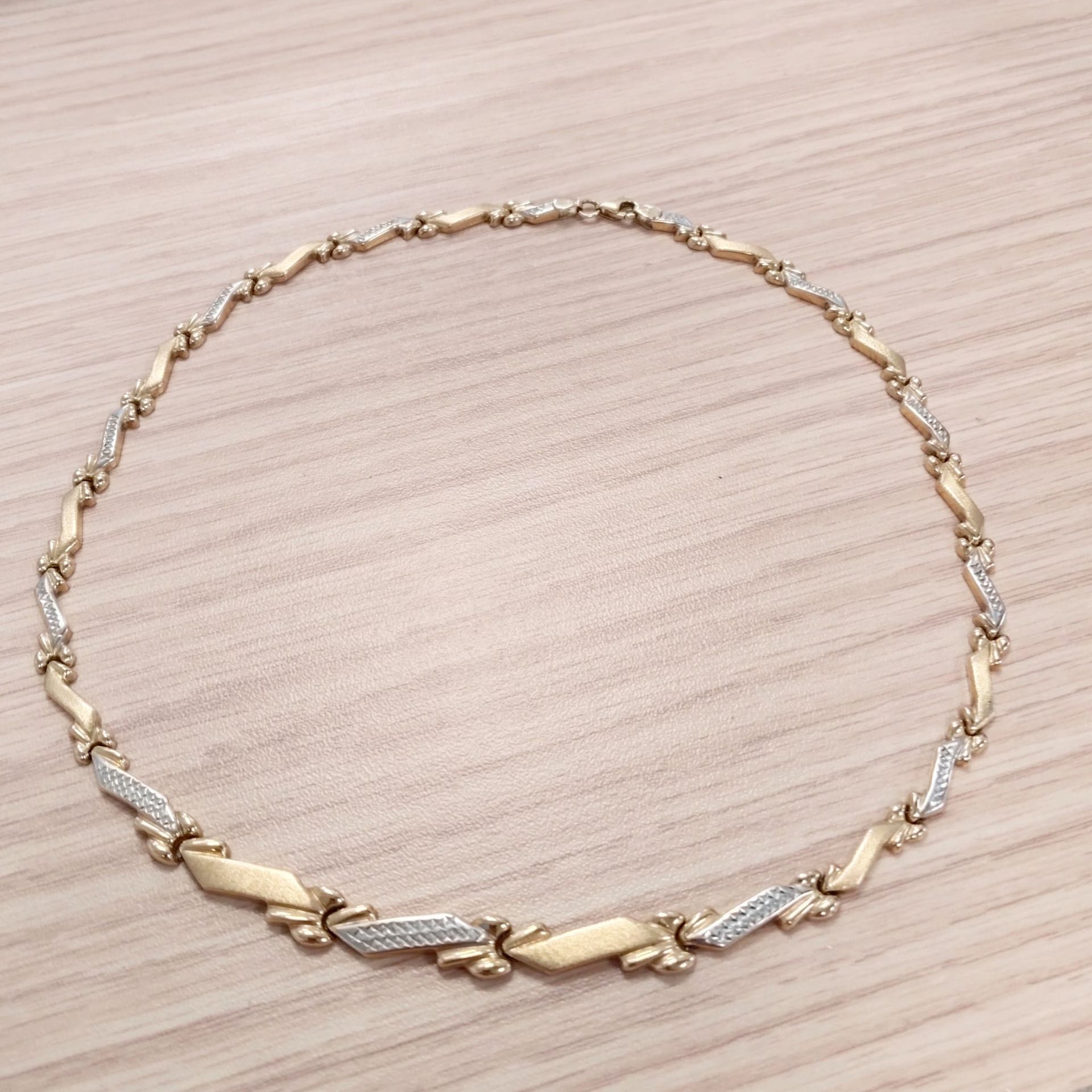 Pulsera de cadena de oro y plata dispuesta en círculo sobre una superficie de madera clara.
