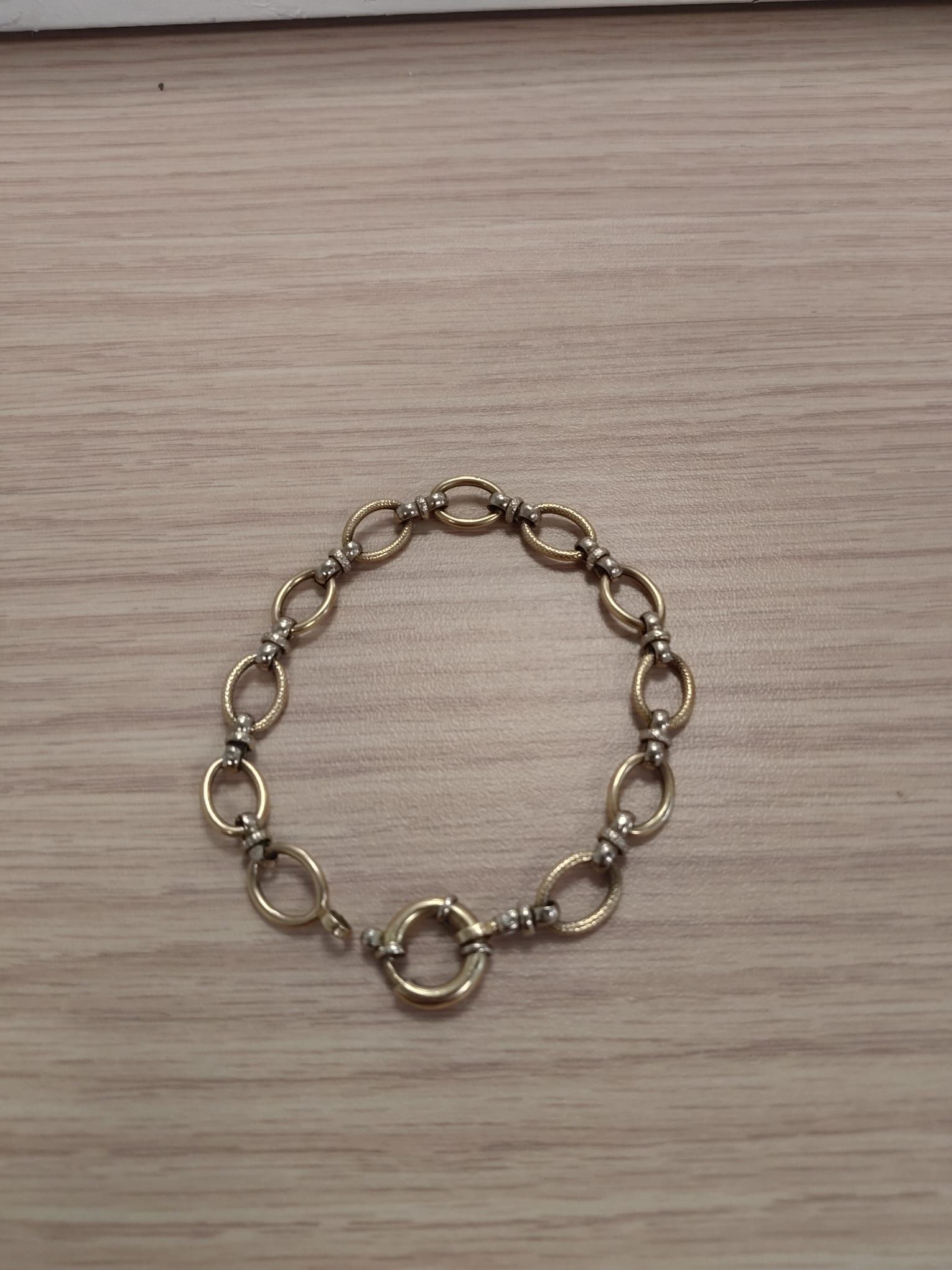 Pulsera de cadena dorada con eslabones ovalados sobre una superficie de madera clara.
