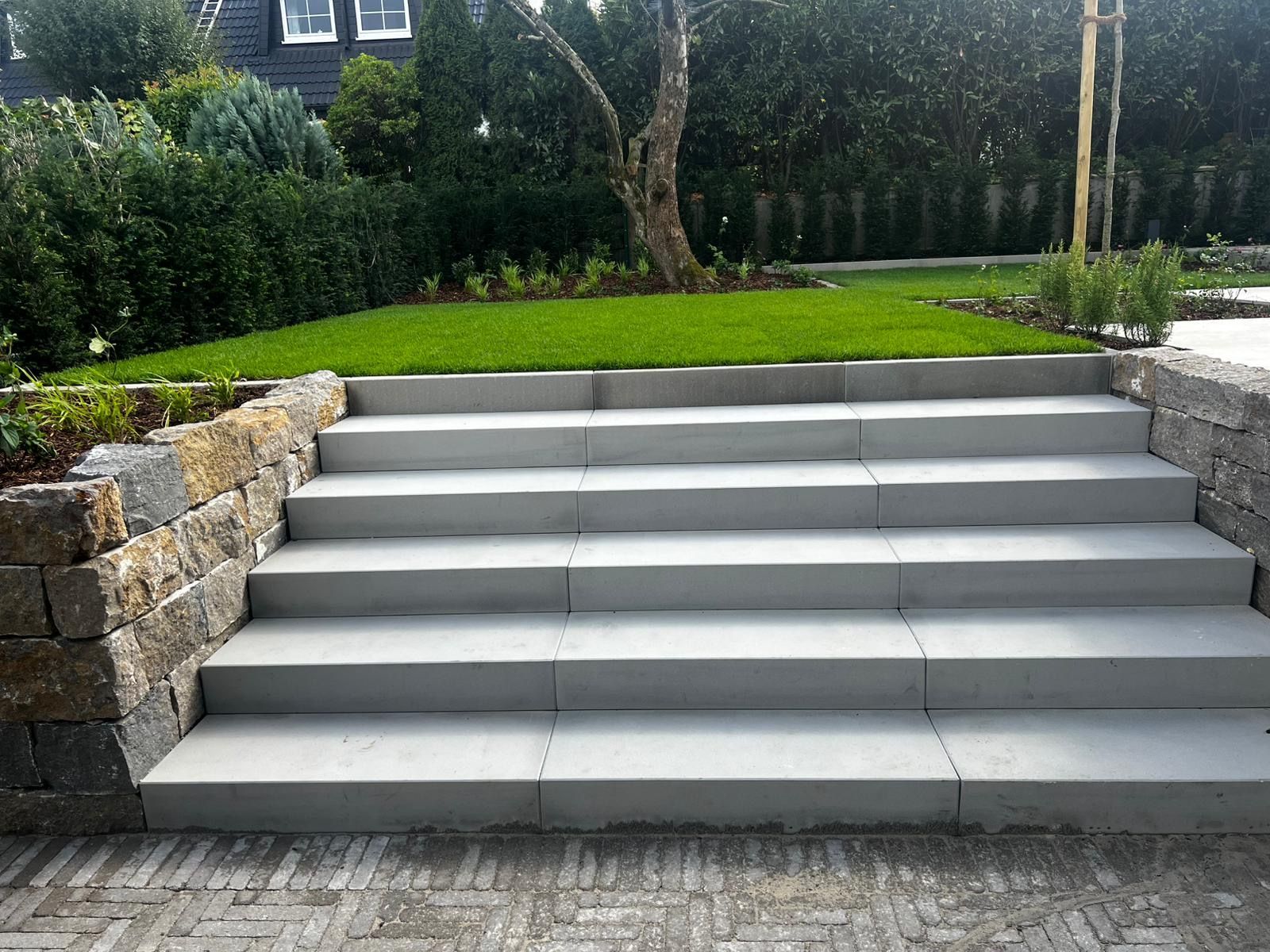 Graue Steinstufen führen zu einer Rasenfläche mit Steinmauern auf beiden Seiten.