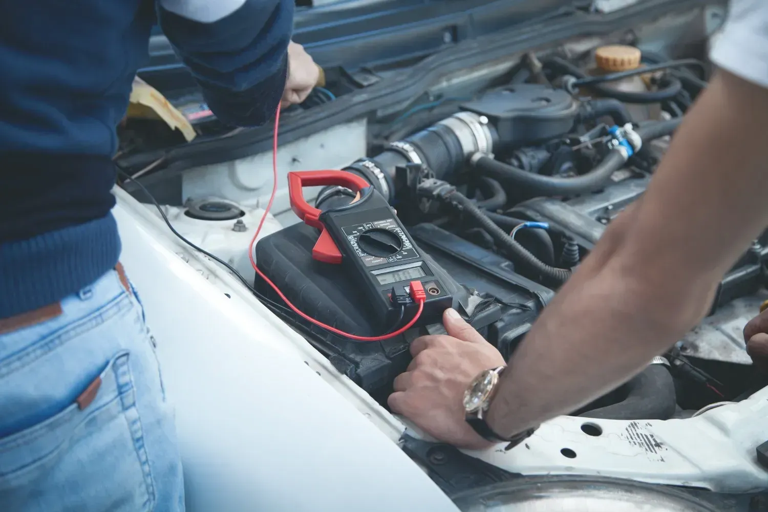 Mecánico utilizando un multímetro para inspeccionar el cableado en el compartimento abierto del motor de un automóvil.